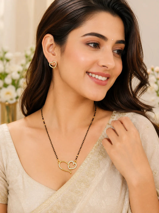 Woman wearing a gold necklace with a heart pendant and matching earrings.