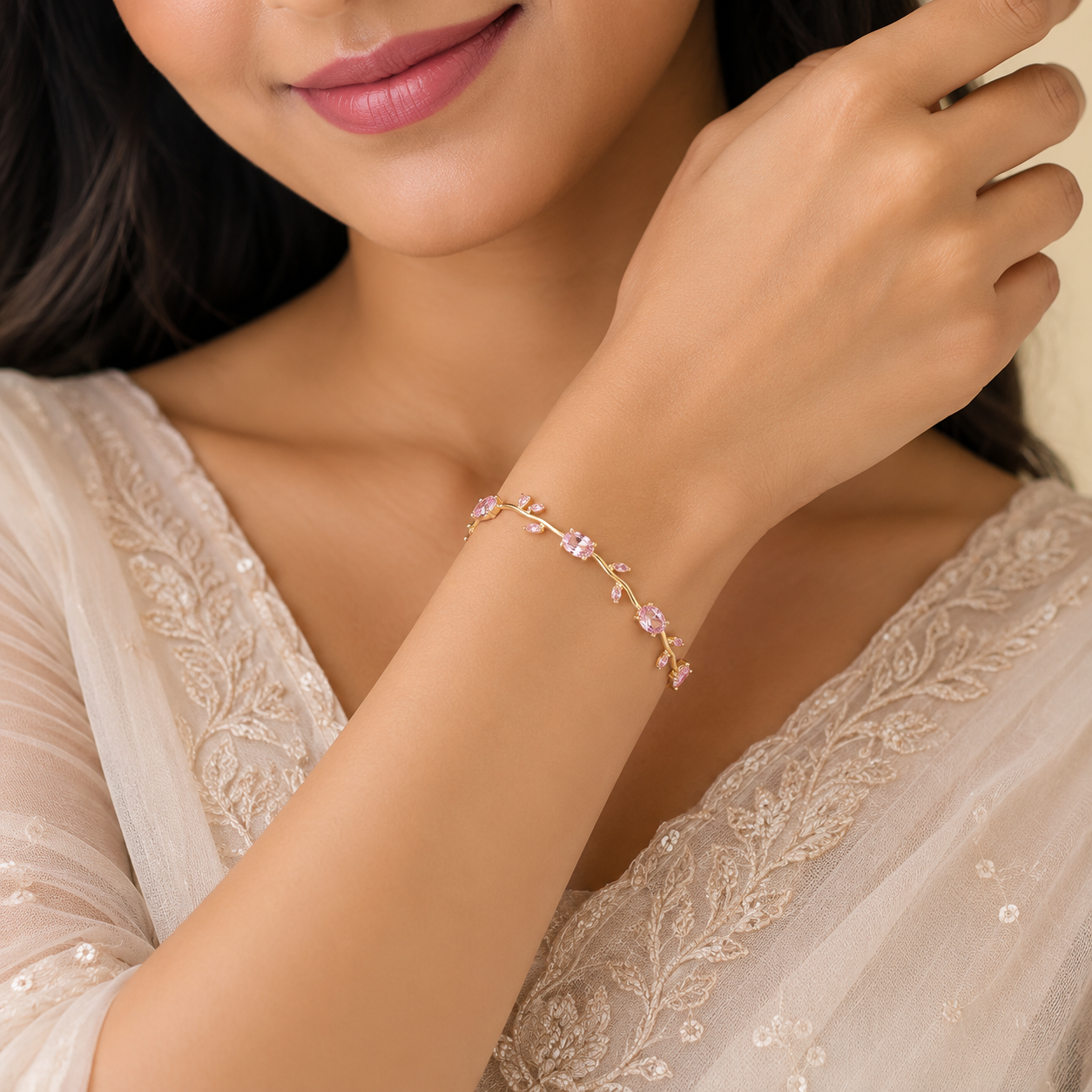 Close-up of a woman's hand wearing a delicate bracelet with pink gemstones, against a neutral background.