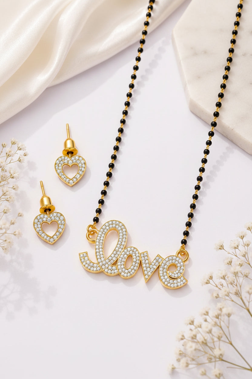 Gold 'love' necklace and heart-shaped earrings on a purple surface with white flowers.