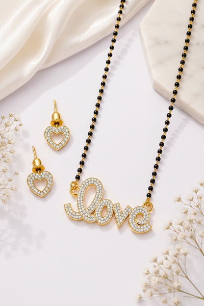 Gold 'love' necklace and heart-shaped earrings on a purple surface with white flowers.